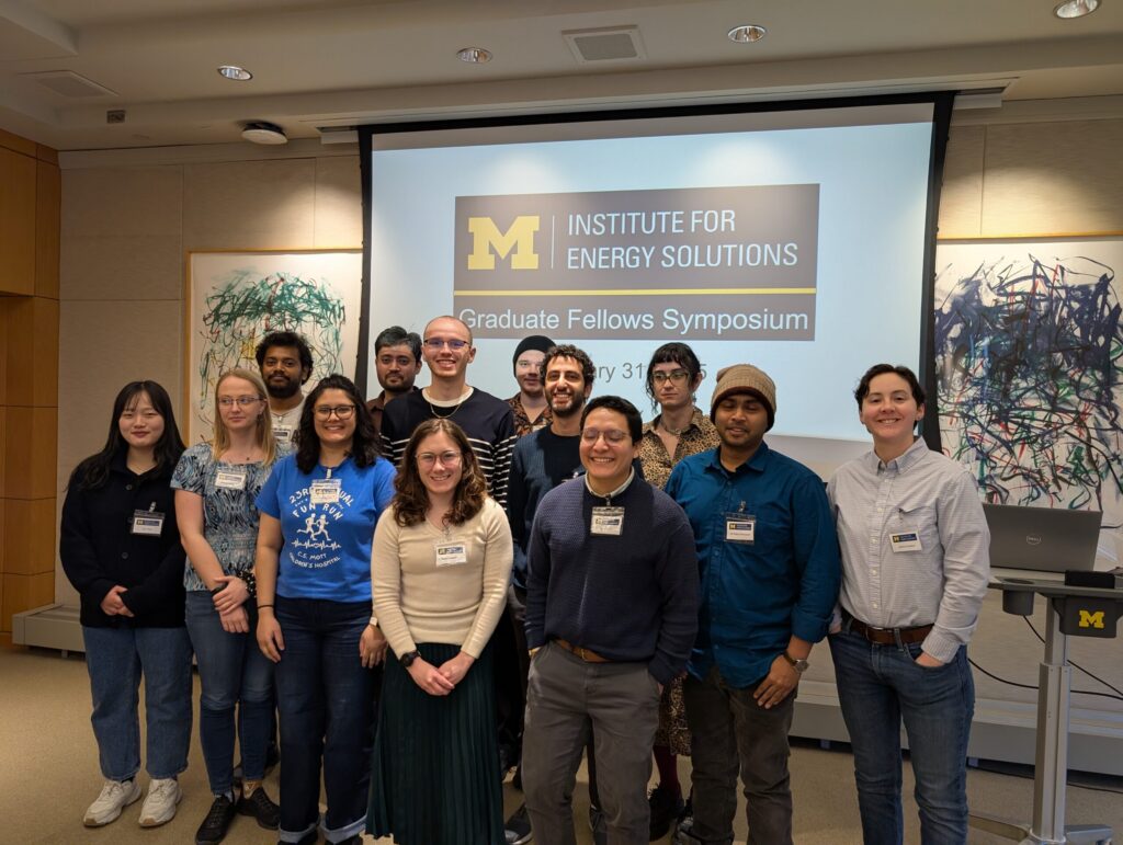 Graduate fellows pose for a group photo in front of a screen displaying the University of Michigan Institute for Energy Solutions Graduate Fellows Symposium.